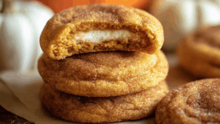 Pumpkin cookies stacked on parchment with one cookie broken to reveal creamy filling